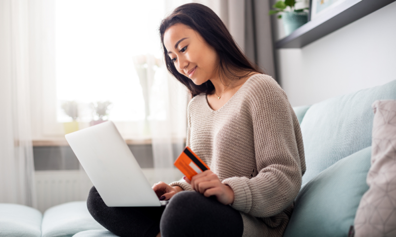 Woman online shopping from her bed, holding an orange credit card