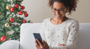 Woman online shopping on mobile phone in front of a christmas tree