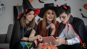 Three people in costume, two as witches and one as a devil, shopping for Halloween over a laptop