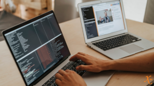 Person coding on one laptop, another laptop open to the side showing a video